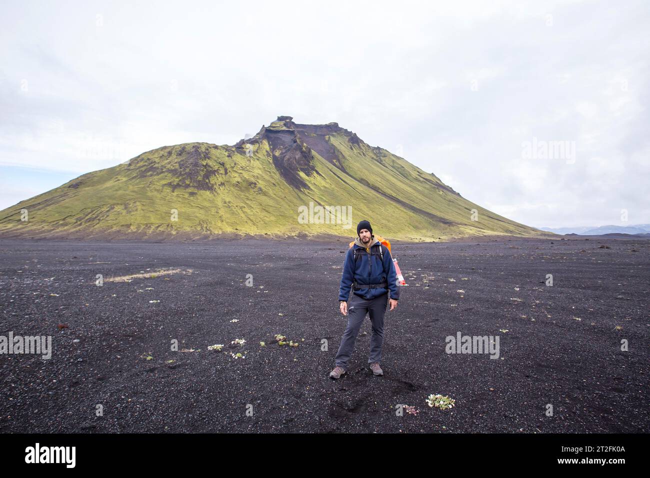 Un giovane in cenere vulcanica e una montagna verde sullo sfondo durante il trekking di 54 km da Landmannalaugar, Islanda Foto Stock