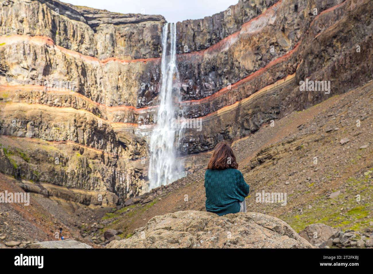 Una giovane ragazza seduta in una delle meraviglie dell'Islanda, la cascata di Hengifoss Foto Stock