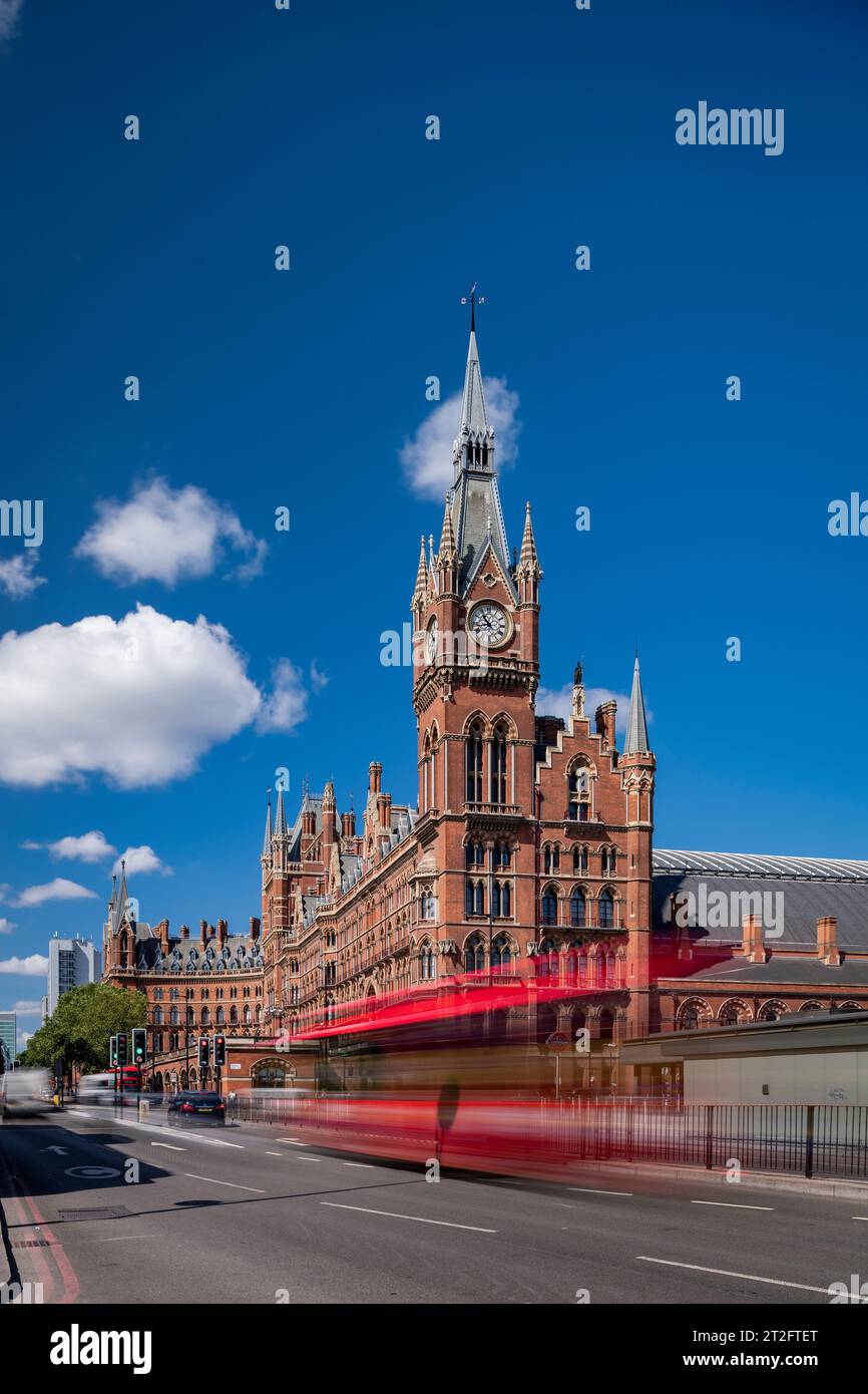Movimento sfocato dell'autobus rosso di Londra fuori dalla stazione internazionale di St Pancras, catturando l'energia della città sotto un cielo blu brillante. Foto Stock