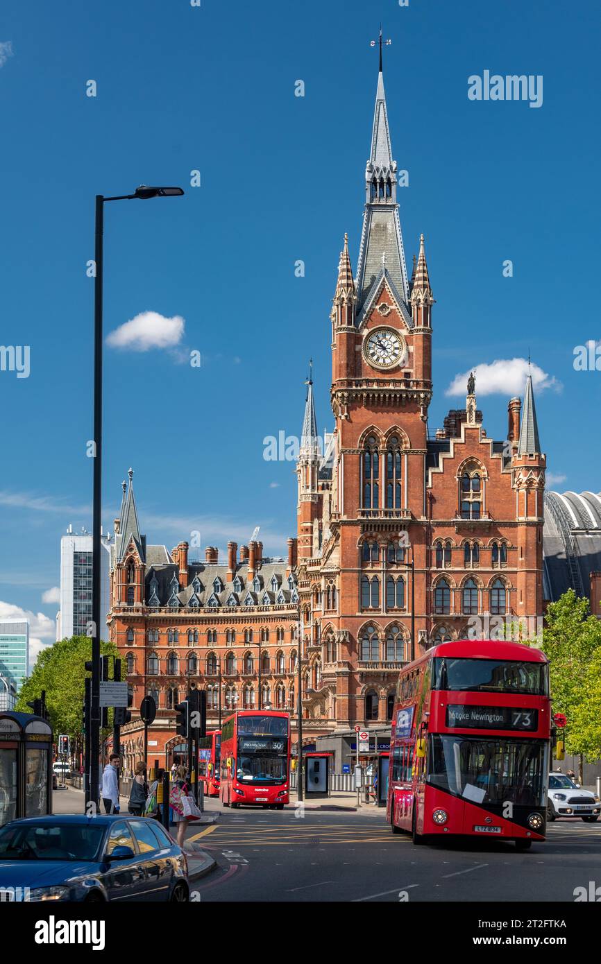 Autobus rossi e vita cittadina fuori St Pancras International, Londra, con la storica facciata in mattoni e cieli azzurri. Foto Stock