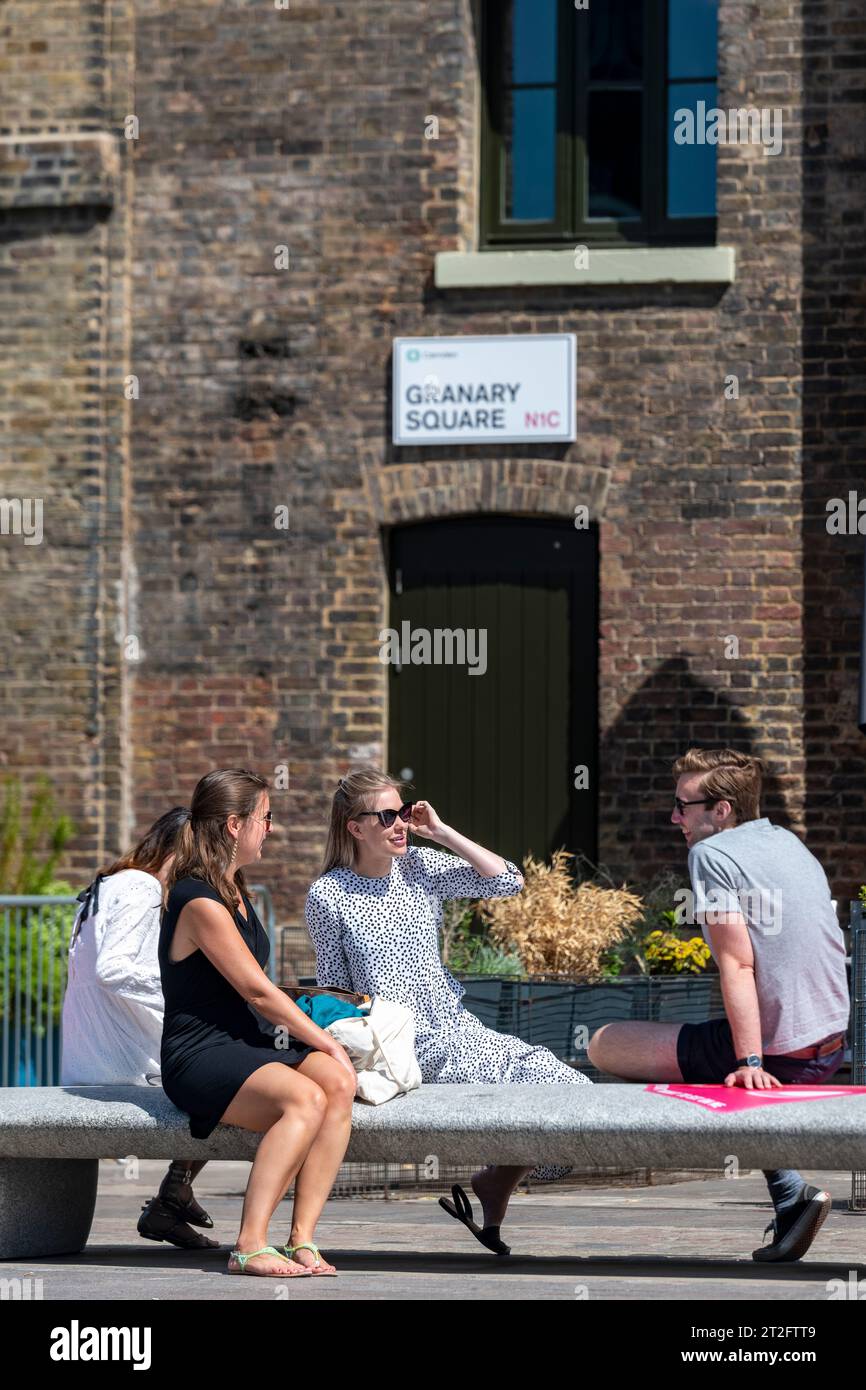 Gruppo di giovani professionisti che si godono il sole durante una pausa pranzo a Granary Square, Kings Cross, Londra in una giornata di sole Foto Stock