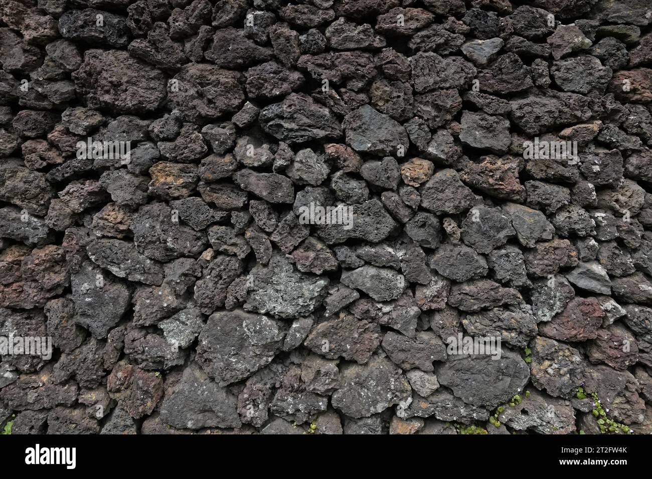 Un muro composto da scure rocce vulcaniche di pietra pomice è mostrato in primo piano, con vista esterna durante il giorno. Foto Stock