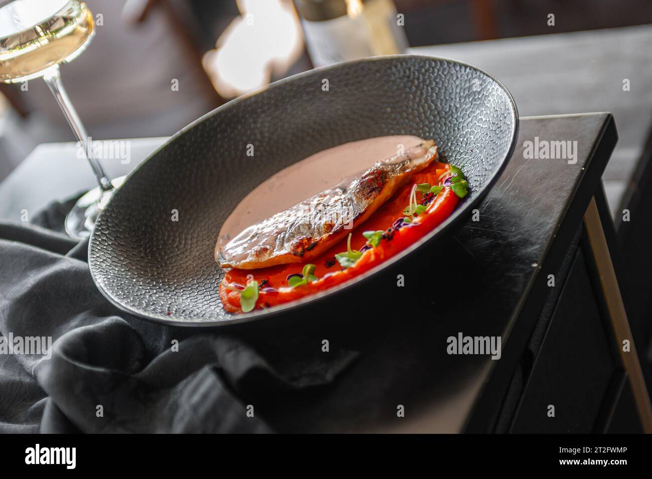 Filetto di spigola o dorado con purea di patate dolci e salsa di uova di pesce volanti su un piatto nero in un ristorante Foto Stock