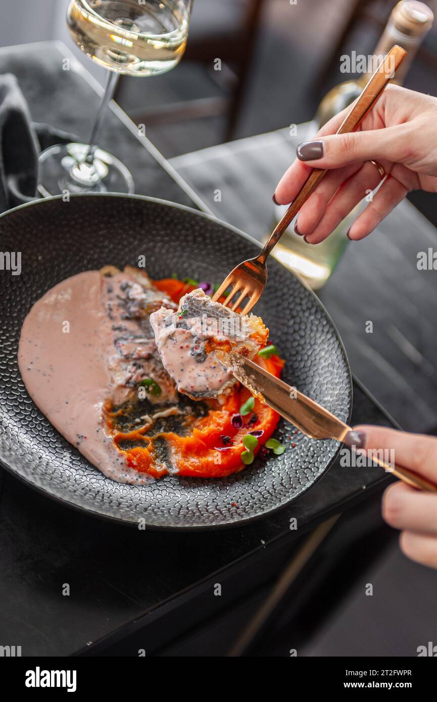 Filetto di spigola o dorado con purea di patate dolci e salsa di uova di pesce volanti su un piatto nero in un ristorante Foto Stock
