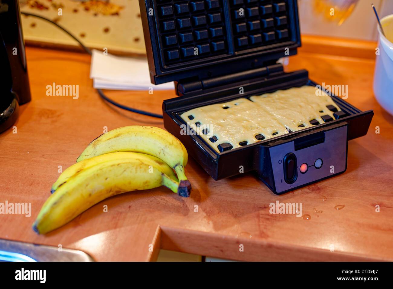 Impasto per waffle in un ferro da stiro con le banane come ingrediente. Foto Stock
