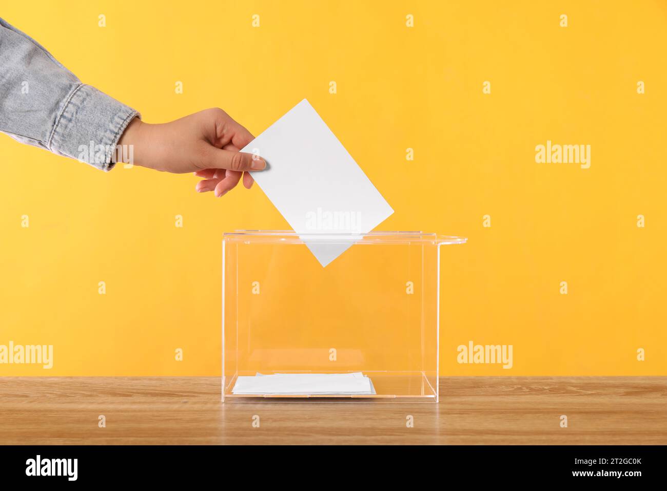 Donna che mette il suo voto nelle urne su un tavolo di legno su sfondo arancione, primo piano Foto Stock