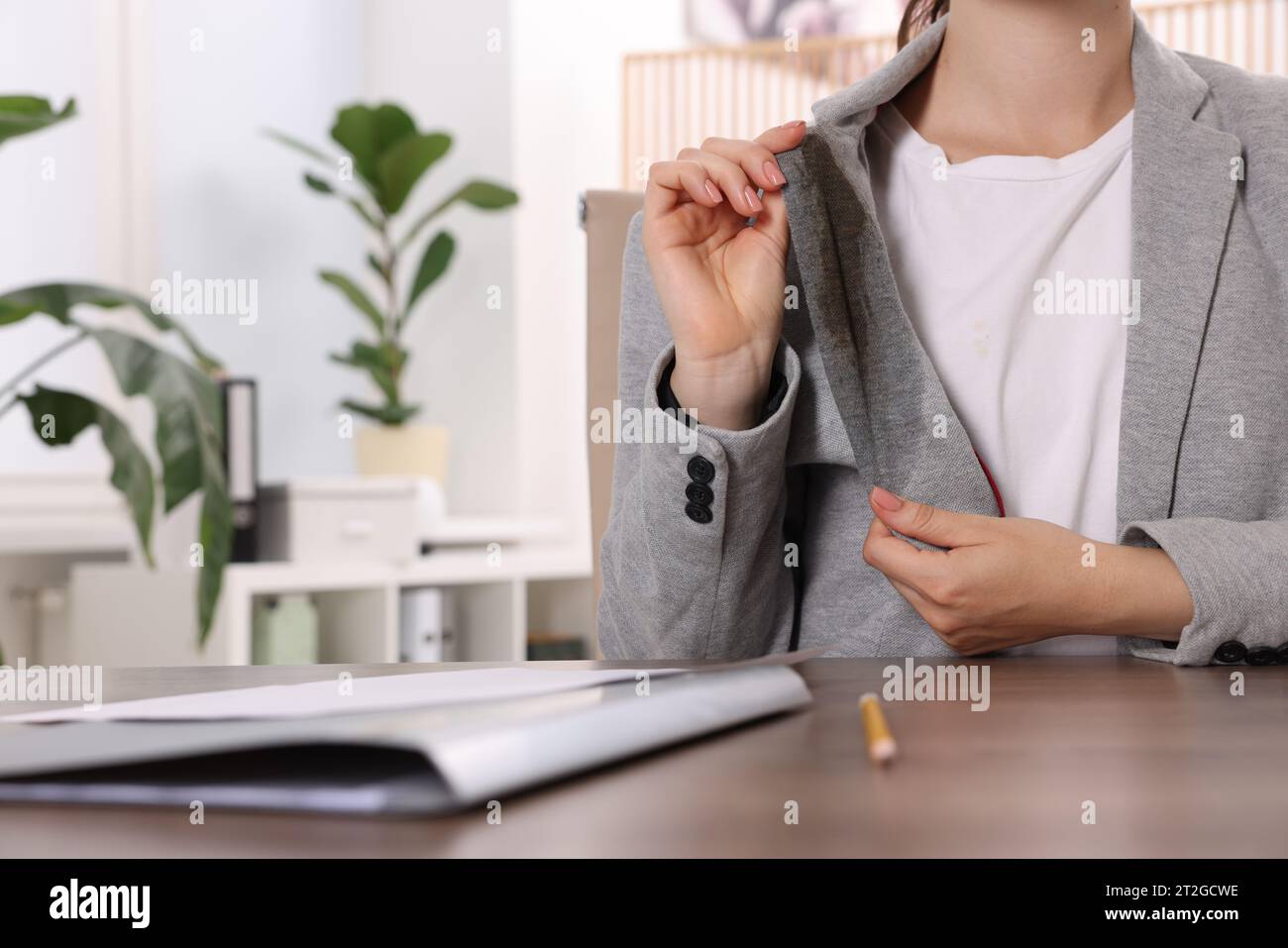 Donna che mostra macchie di caffè sulla giacca al tavolo di legno all'interno, primo piano Foto Stock
