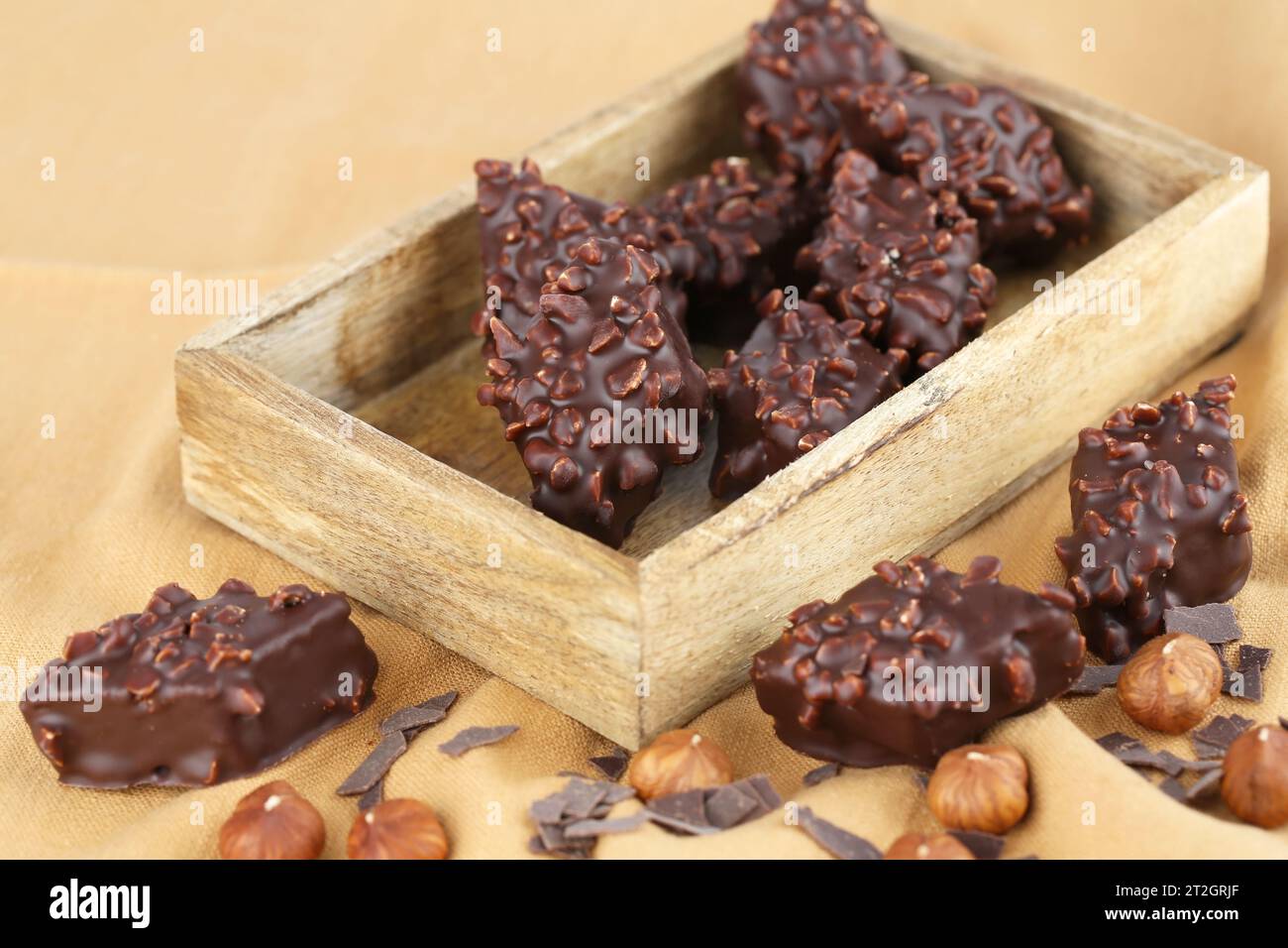 Cioccolato con nocciole in scatola di legno sullo sfondo del tessuto beige. Foto Stock