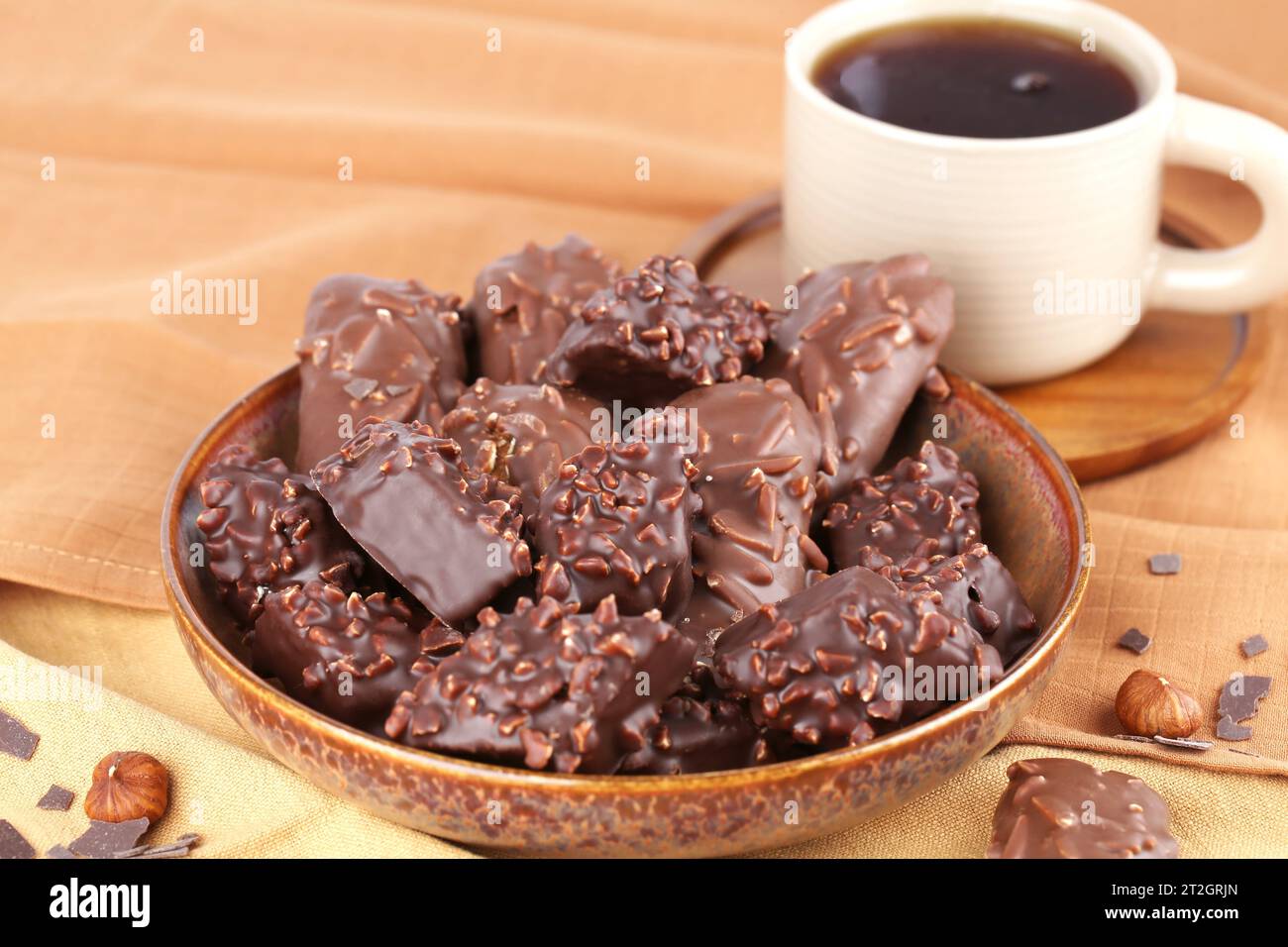 Cioccolato con nocciole in recipiente di ceramica e tazza di tè su sfondo marrone. Foto Stock