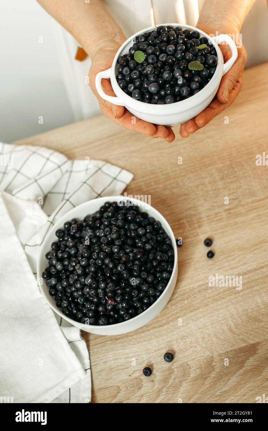 Ci sono piatti di mirtilli maturi sul tavolo della cucina e nelle mani dei donne. Prodotti biologici, vista dall'alto. Foto Stock