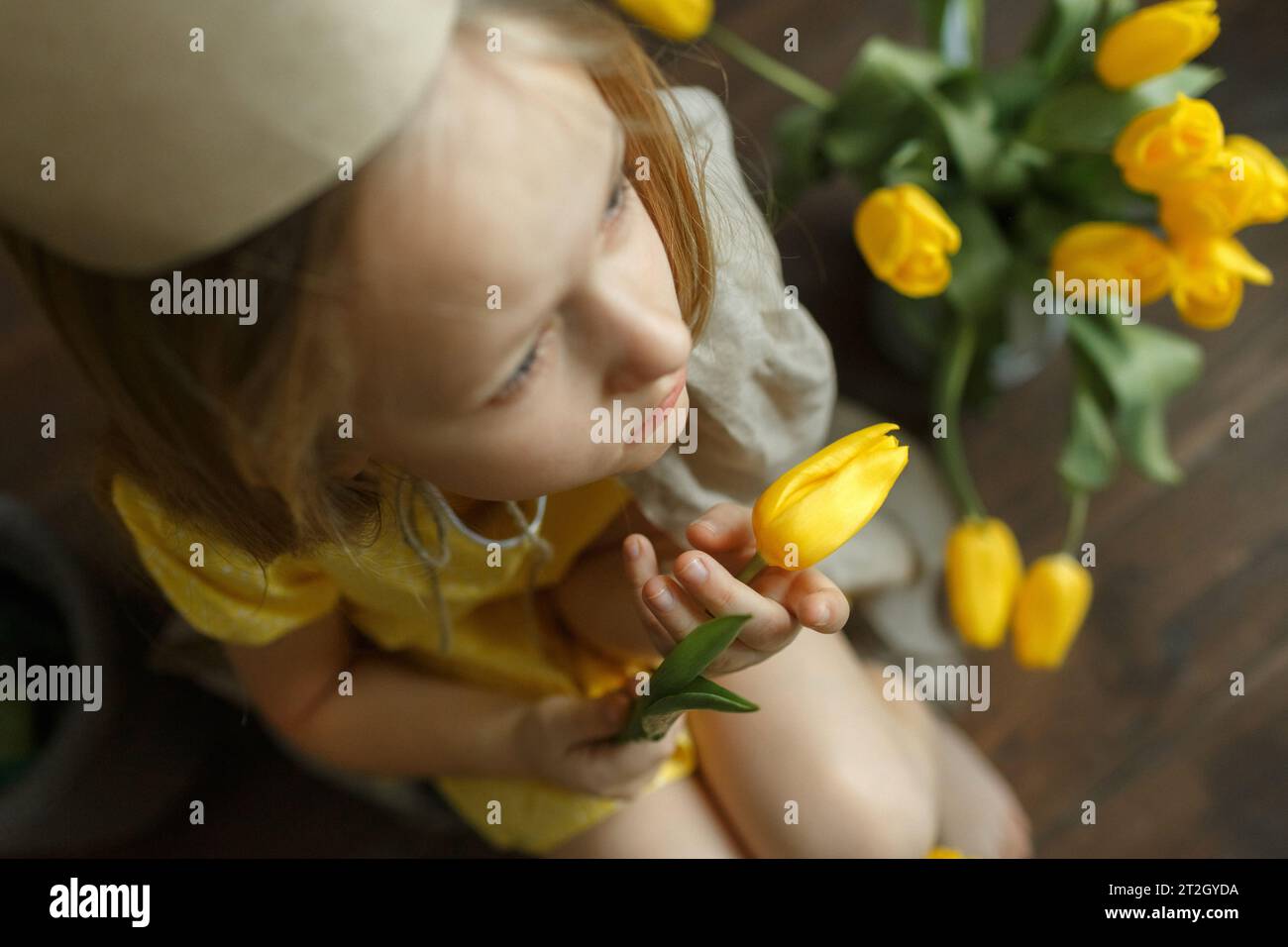 Vista dall'alto di una ragazza che tiene in mano un tulipano e si siede tra i tulipani. Affilatura selettiva. Nitidezza su un tulipano nelle mani. Foto Stock