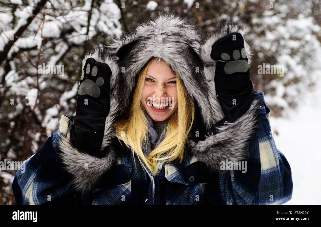 Ragazza felice con cappotto caldo, cappello e guanti nel parco invernale innevato. Donna sorridente in abiti alla moda all'aperto. Clima freddo. Bella modella femminile in pelliccia Foto Stock