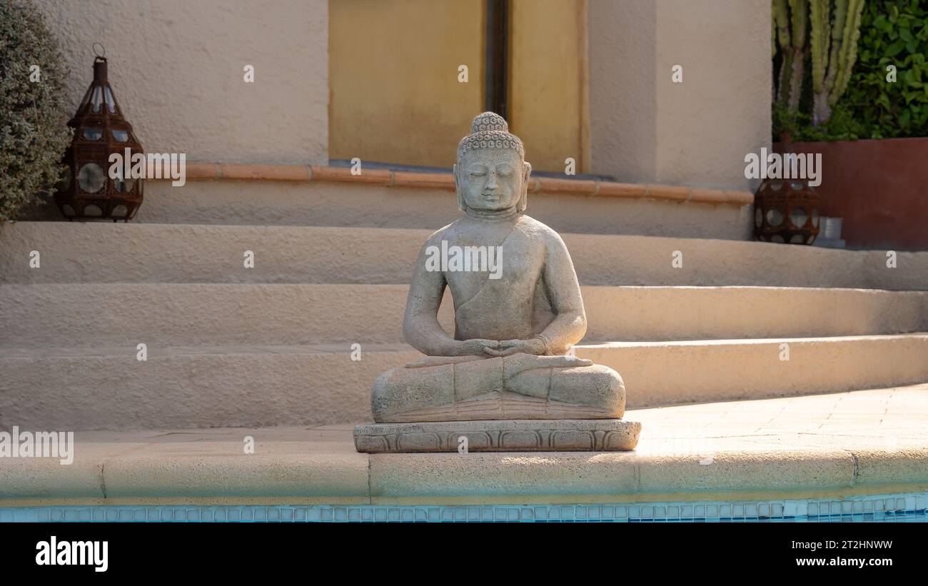 Statua del Buddha accanto a una piscina con una casa mediterranea sullo sfondo Foto Stock