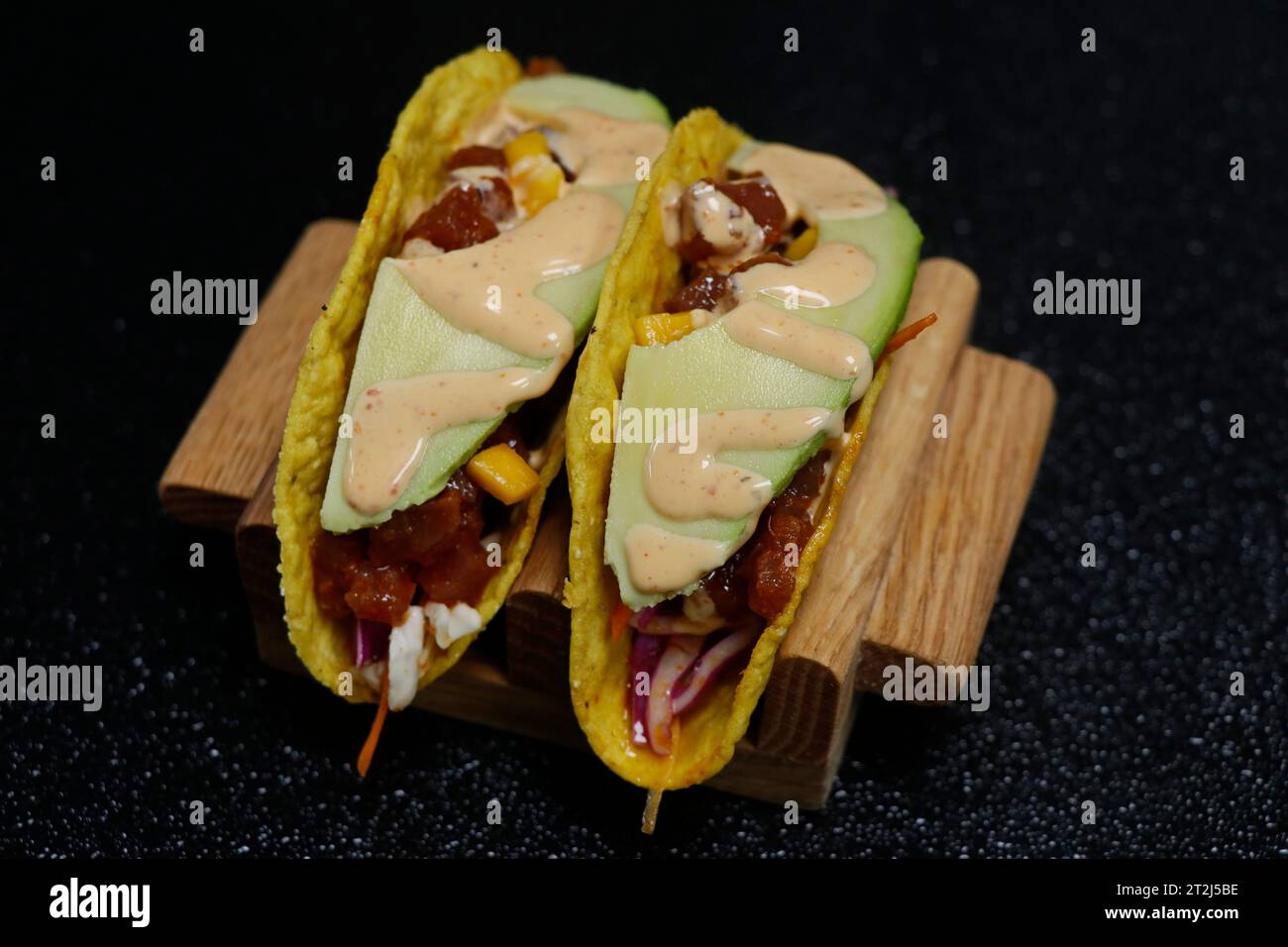 taco di mais messicano con tonno e salmone ripieni e guarnire con avocado e mango su fondo nero Foto Stock