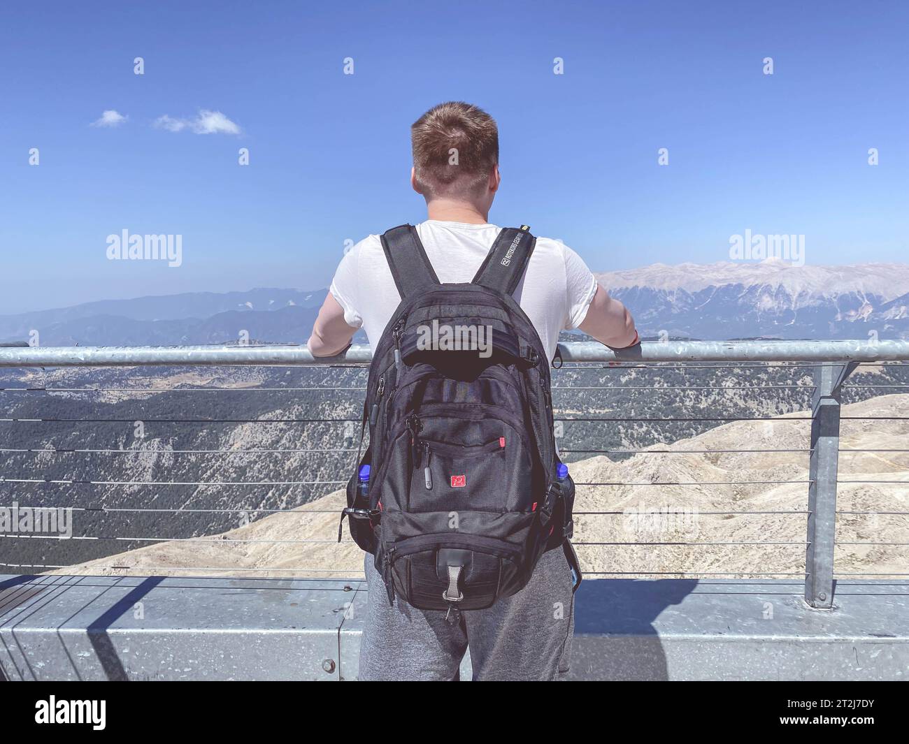 un uomo con un grande zaino nero si trova su una piattaforma di osservazione in cima a una montagna. turista in un paese caldo. vacanze attive in montagna. Foto Stock