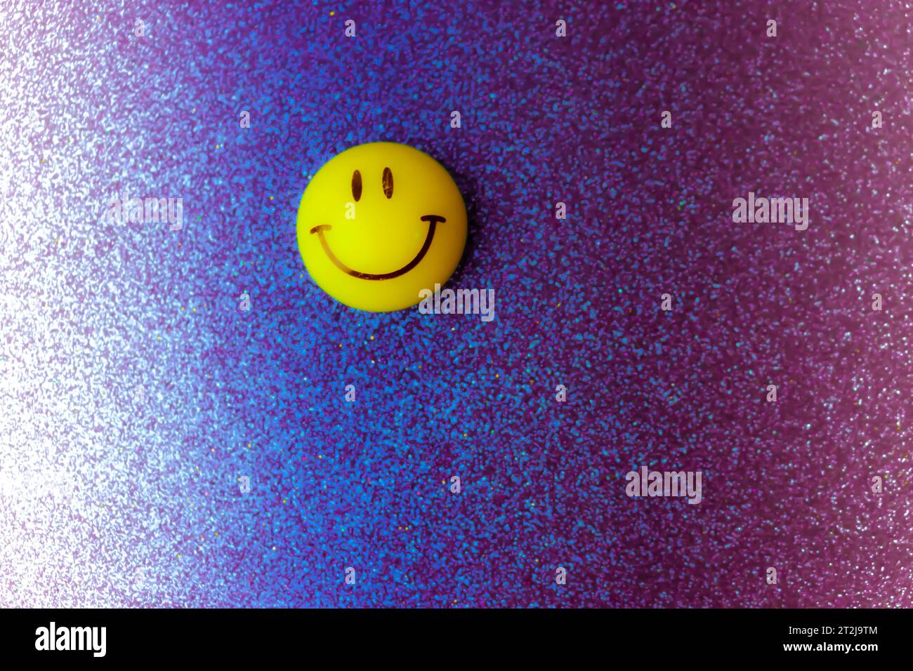 Giocattolo rotondo sorridente sorridente di plastica giallo Emoji con faccia rotonda su sfondo blu. Foto Stock