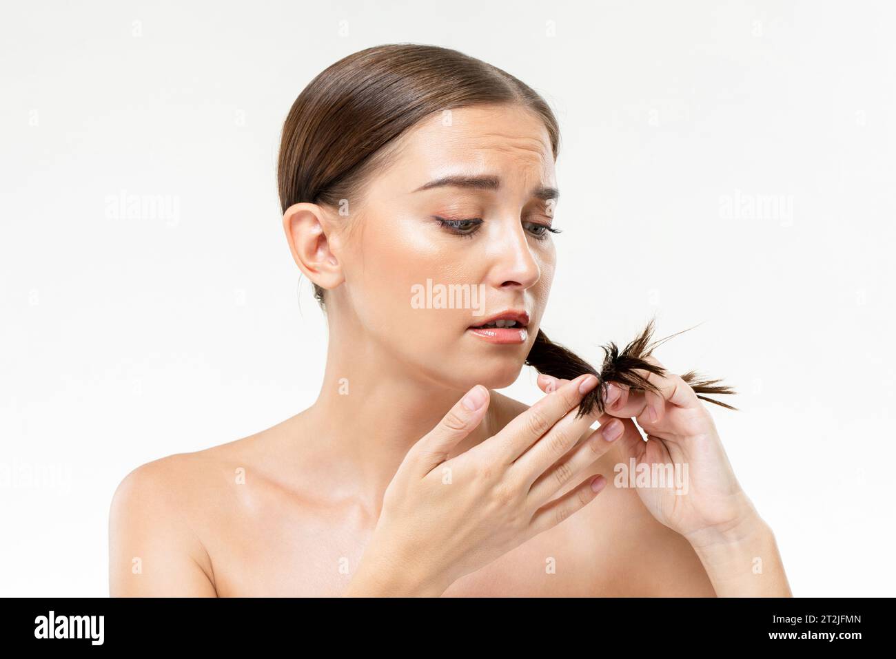 Giovane donna insoddisfatta che tocca e ispeziona le doppie punte durante la routine di cura dei capelli su sfondo bianco Foto Stock