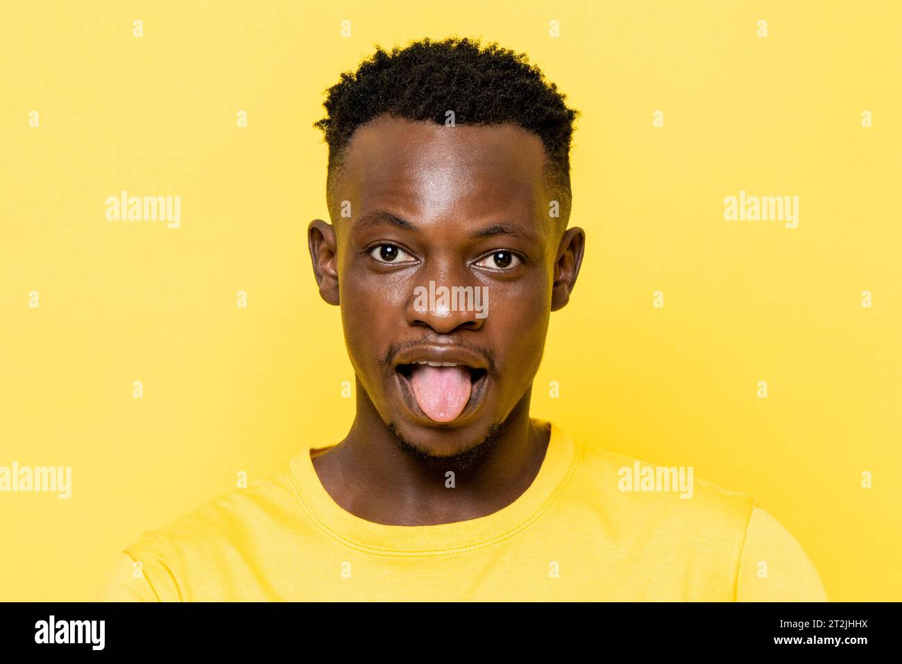 Un uomo africano che sporge la lingua su uno sfondo giallo in uno studio leggero Foto Stock