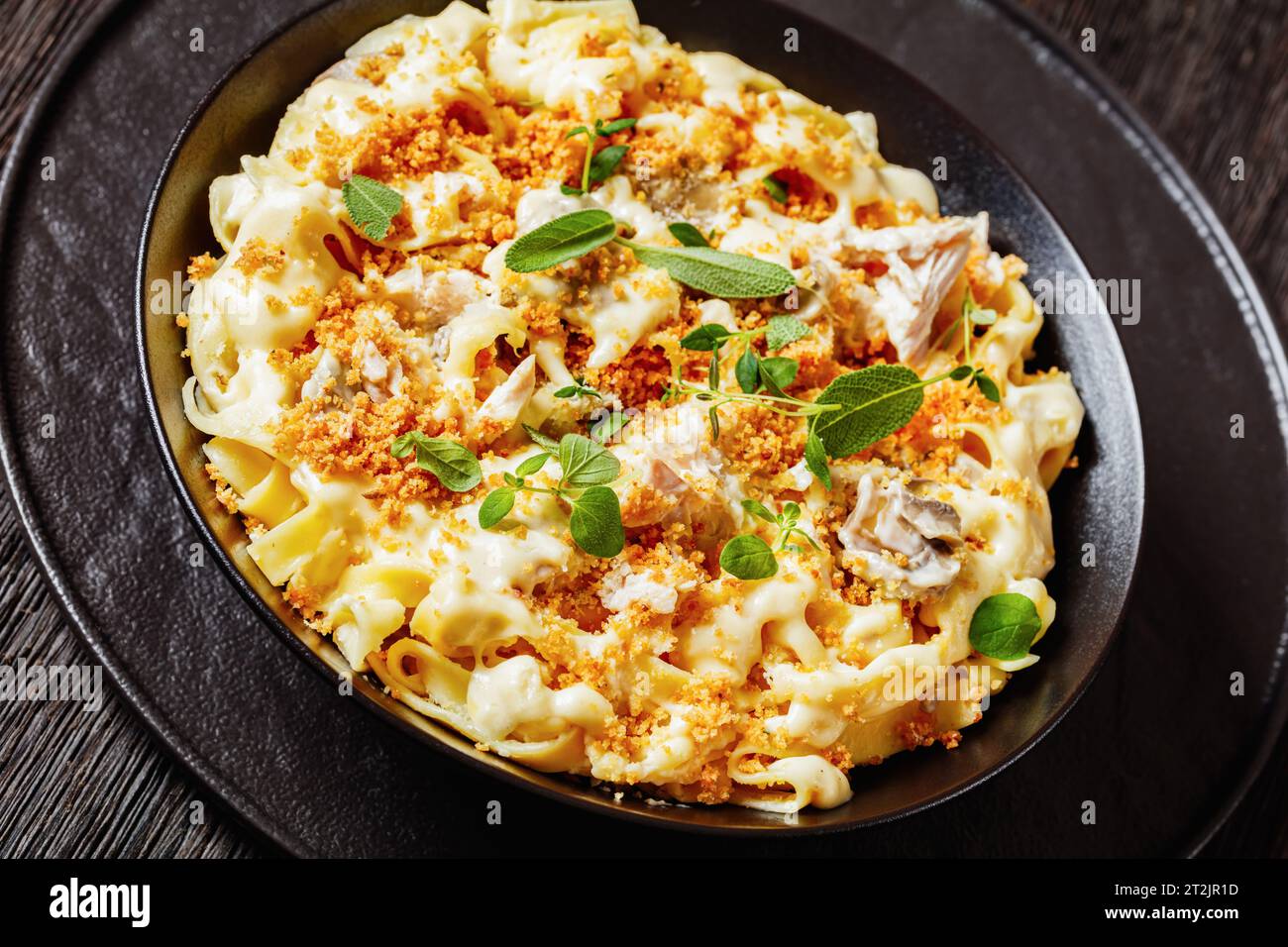 primo piano della cremosa tagliatelle di pollo e funghi condita con pangrattato ed erbe fresche in una ciotola nera su un tavolo di legno scuro Foto Stock