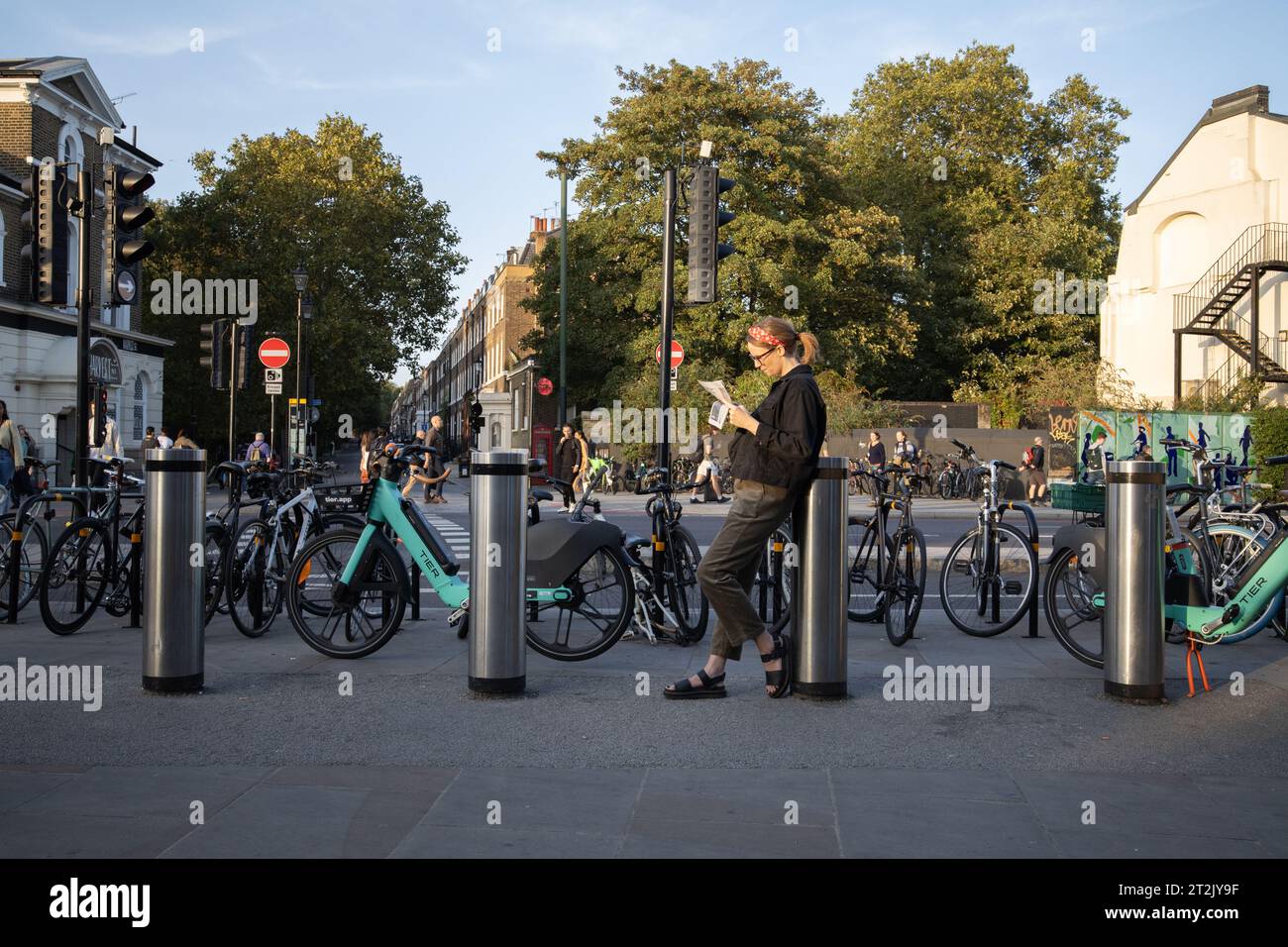 Una donna che legge il suo libro al sole della sera d'autunno fuori dalla stazione della metropolitana di Highbury & Islington, Londra, Inghilterra, Regno Unito Foto Stock
