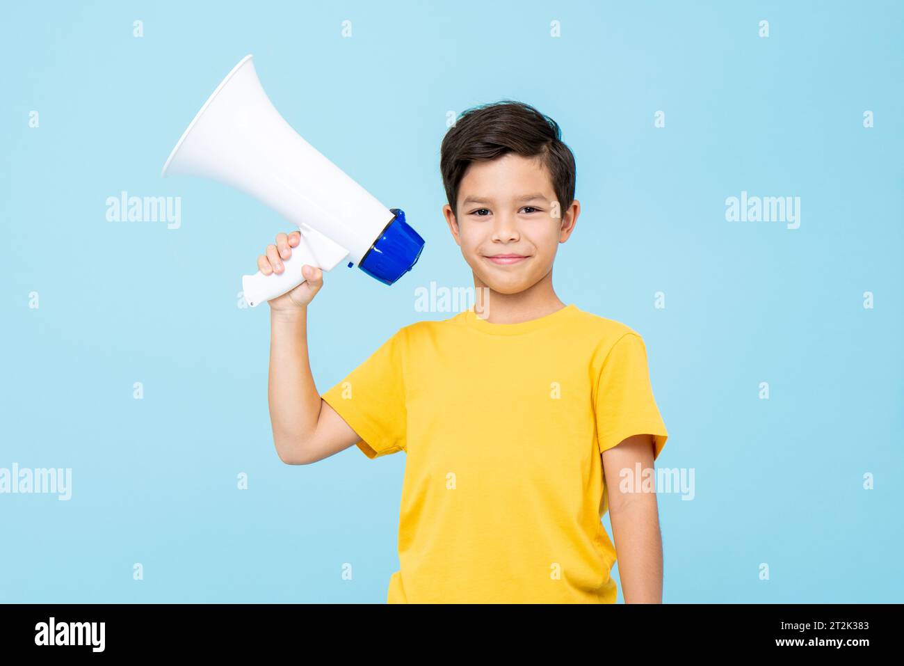 Simpatico bambino che tiene in mano il megafono su uno sfondo blu chiaro isolato in studio Foto Stock