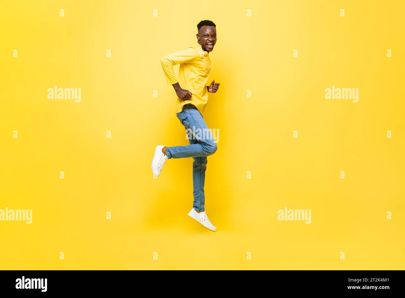 Ritratto a tutta lunghezza dell'eccitato uomo africano che salta su uno sfondo isolato di colore giallo da studio Foto Stock