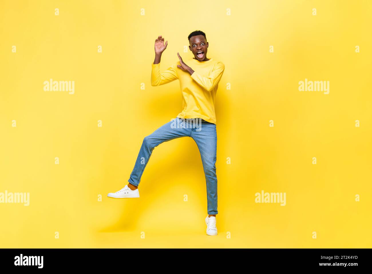 Scioccato uomo africano che salta con le mani alzate in uno sfondo isolato di colore giallo studio Foto Stock