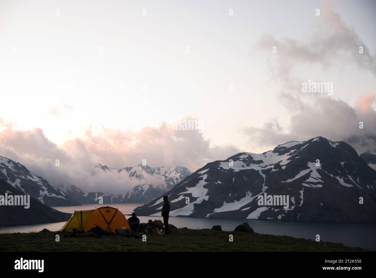 Due uomini si godono l'ultima luce della giornata dal campeggio vicino ad un alto lago alpino. Foto Stock