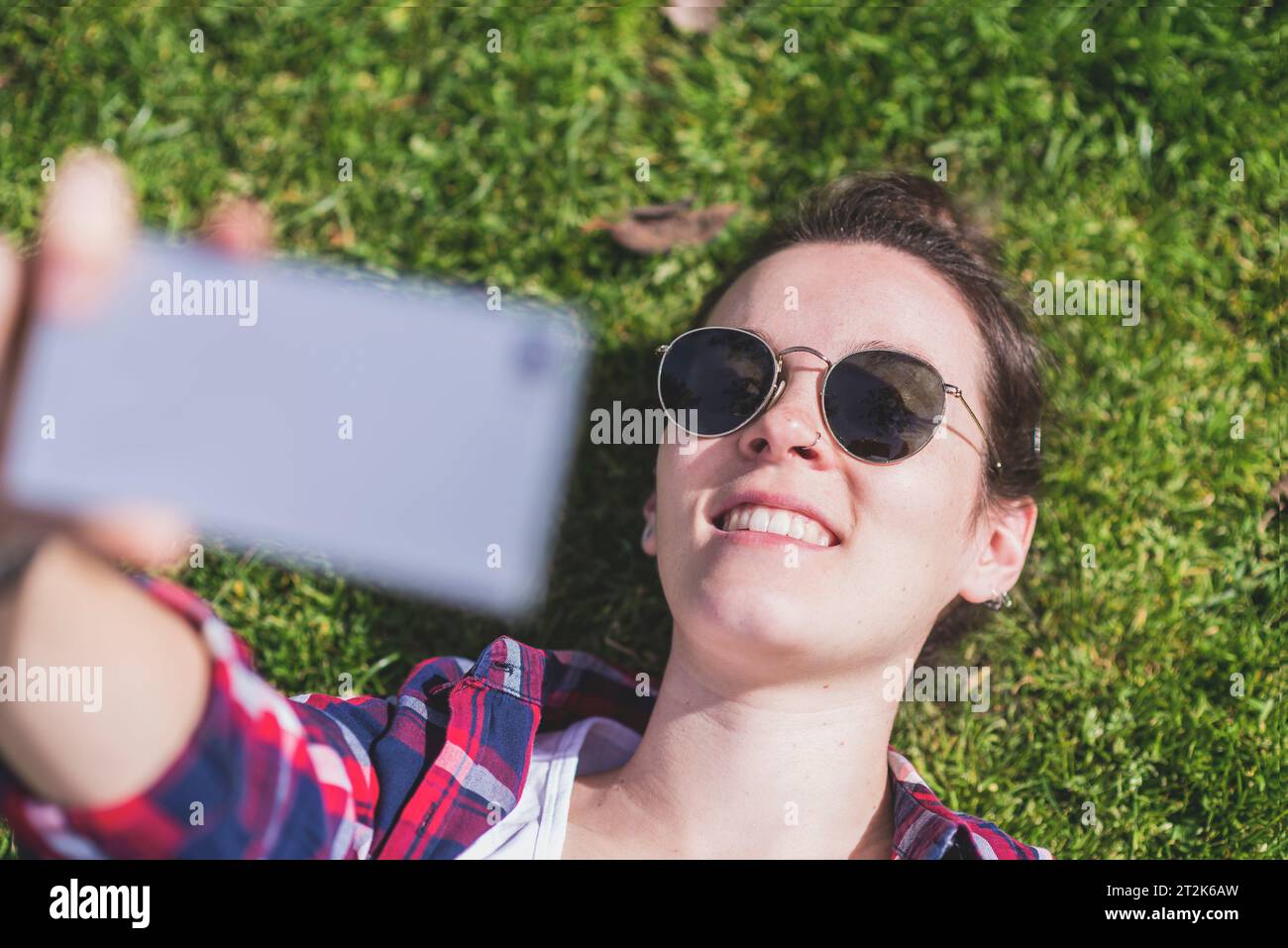 Sopra la vista di una giovane donna hipster sorridente sdraiata sull'erba in una Foto Stock