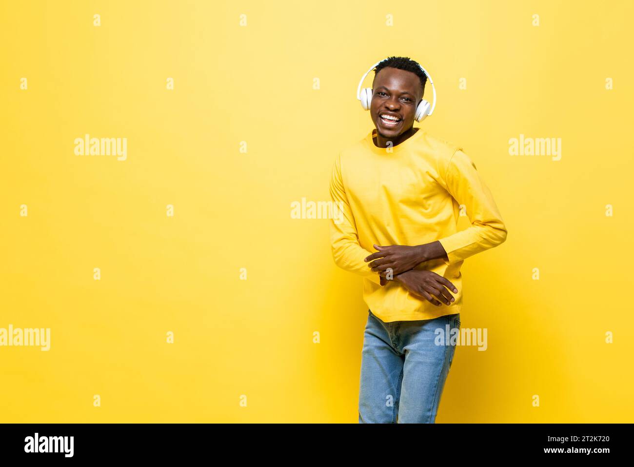 Un uomo africano felice e positivo che ascolta musica con le cuffie in uno studio di colore giallo, sfondo isolato con spazio per la copia Foto Stock