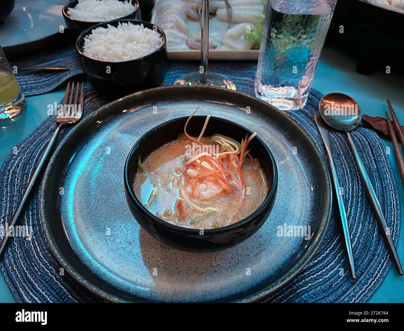 Vista dall'alto di una gustosa e piccante zuppa tailandese di pesce Tom Yum servita in una ciotola nera per cena. Foto Stock