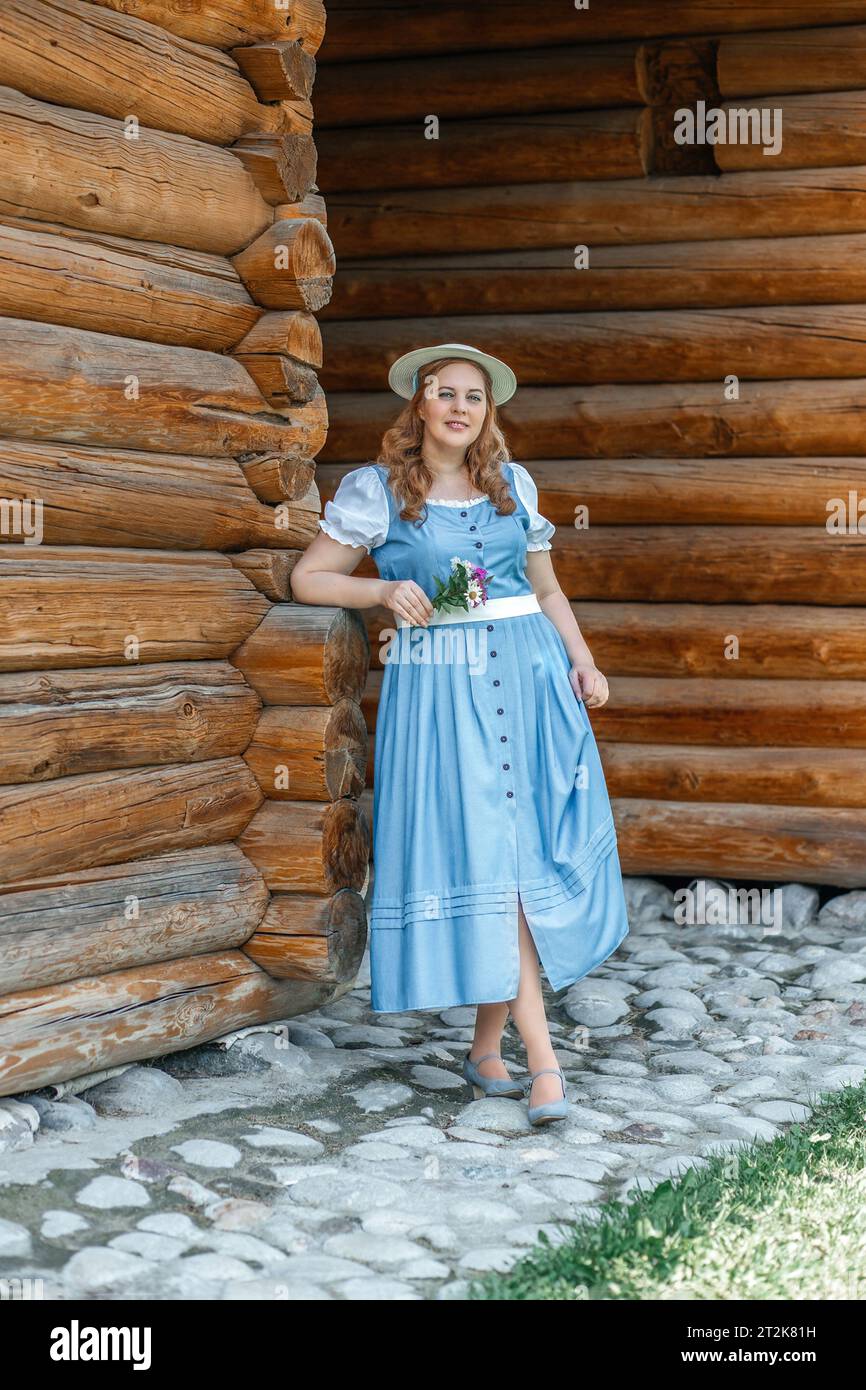 Una donna in abito blu retrò con mele raccolte in grembiule si trova nel cortile di un giardino, un orto. Stile di vita biologico rustico, agri Foto Stock