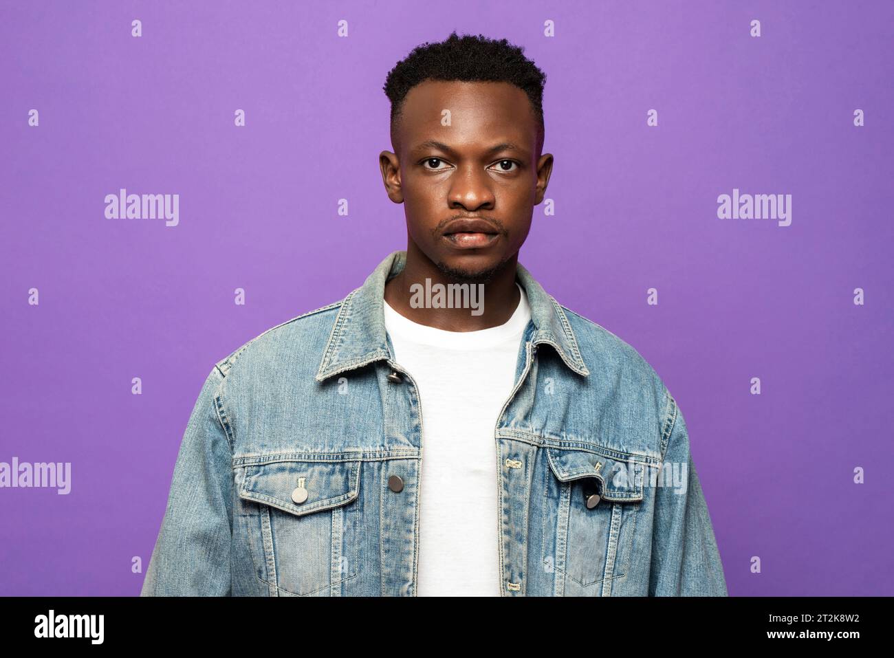 Ritratto del volto di un giovane uomo africano che guarda la fotocamera in uno studio di colore viola con sfondo isolato Foto Stock