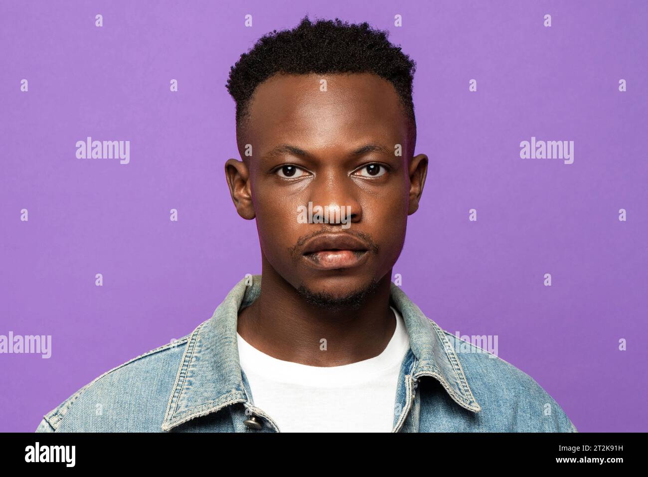 Ritratto del volto di un giovane e affascinante uomo africano che guarda la fotocamera su uno sfondo isolato in uno studio di colore viola Foto Stock