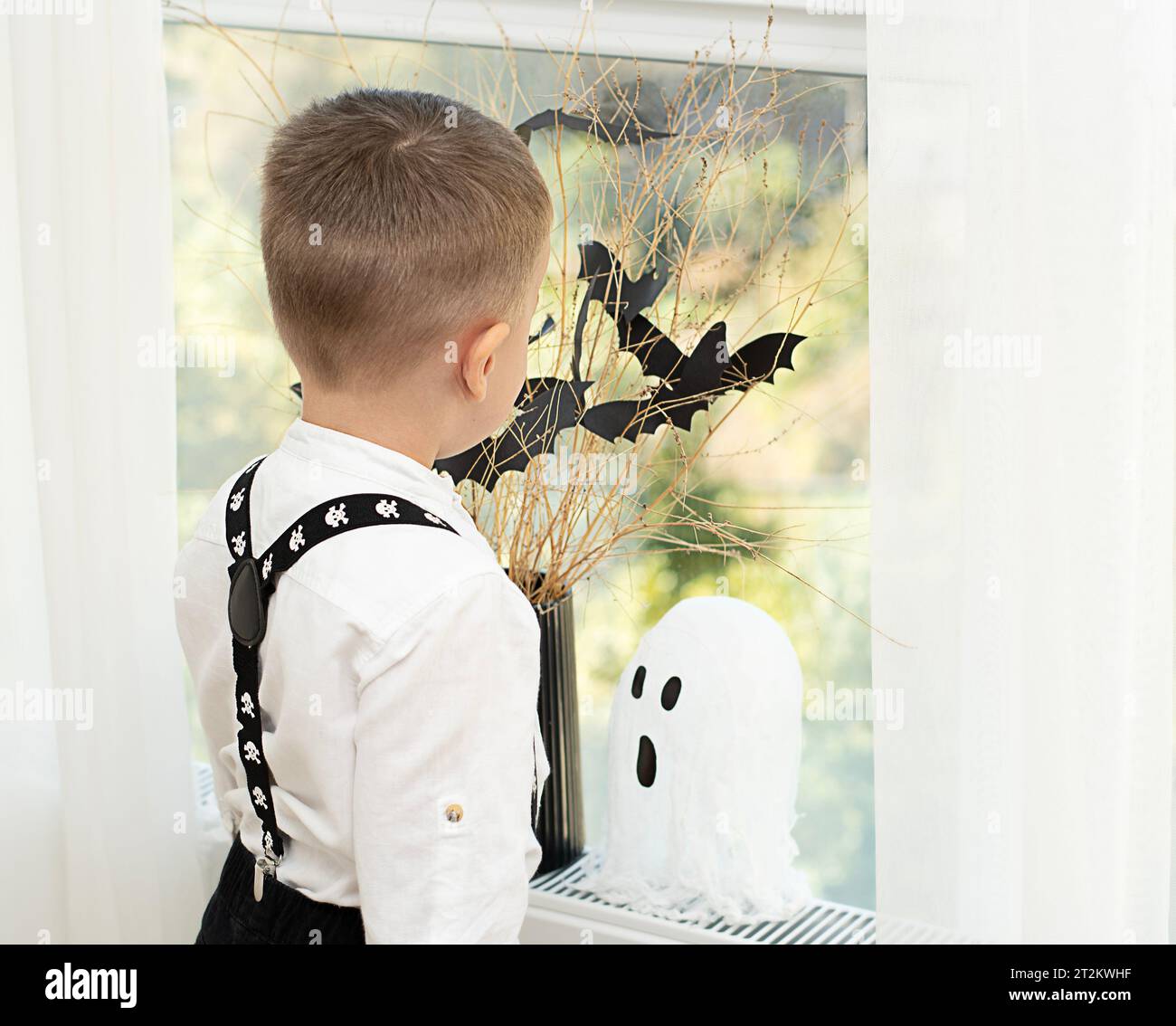 Concetto di Halloween. Niente faccia. Le mani del bambino vicino alla finestra, sullo sfondo di un vaso con rami asciutti e pipipistrelli di carta nera. Primo piano Foto Stock