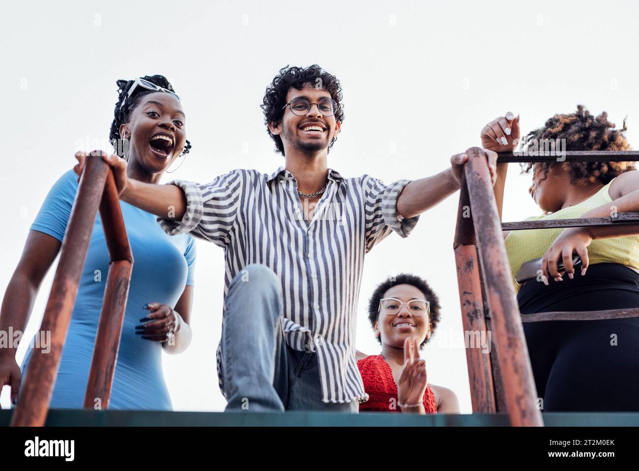 Quattro allegri amici multietnici scendono la scala di ferro dal tetto della casa. Affascinanti donne africane e un uomo di razza mista si divertono e si divertono Foto Stock