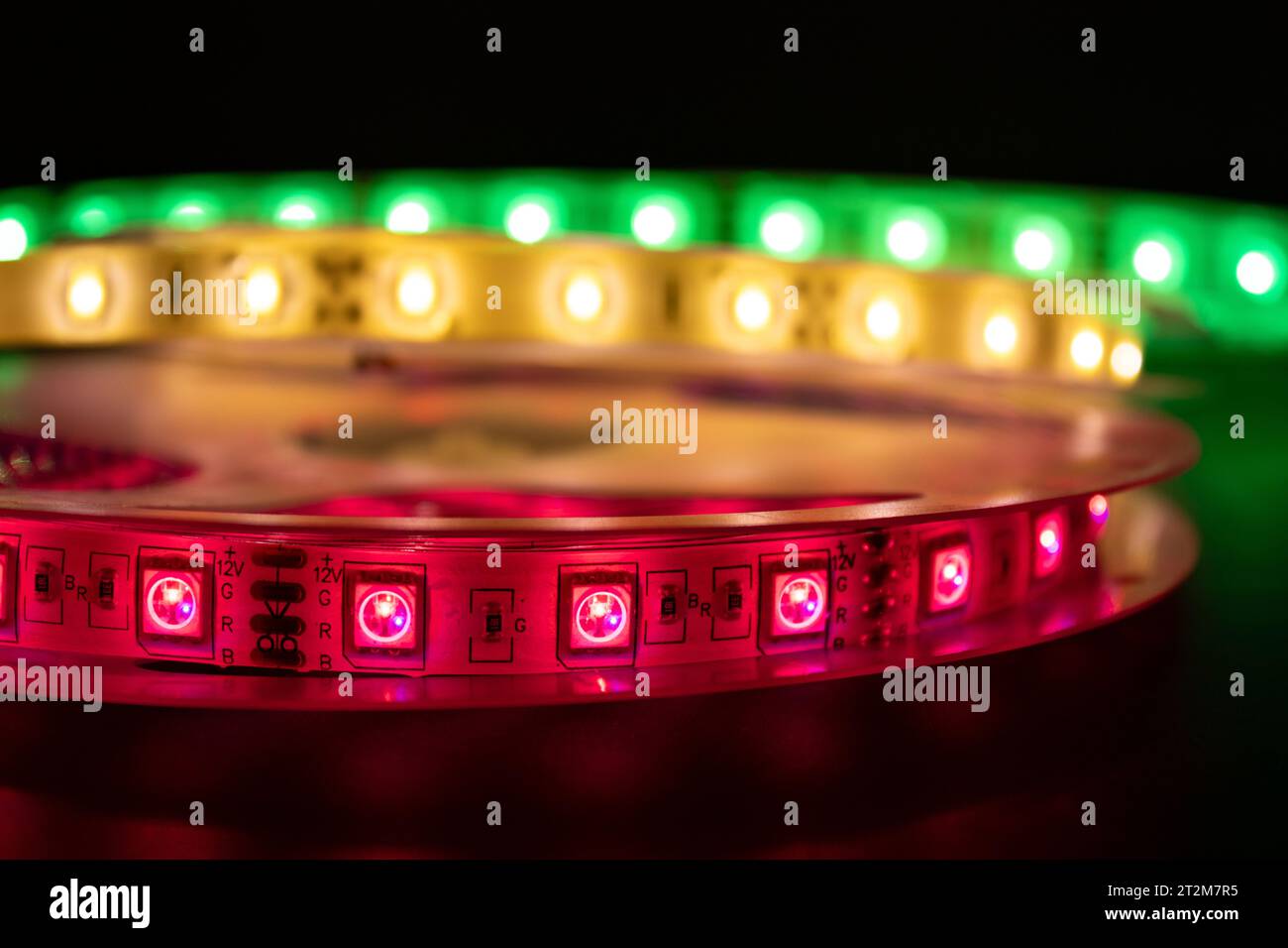 Bobina con rotolo di strisce luminose LED luminose posizionate sul tavolo, colore rosa, verde e bianco caldo Foto Stock