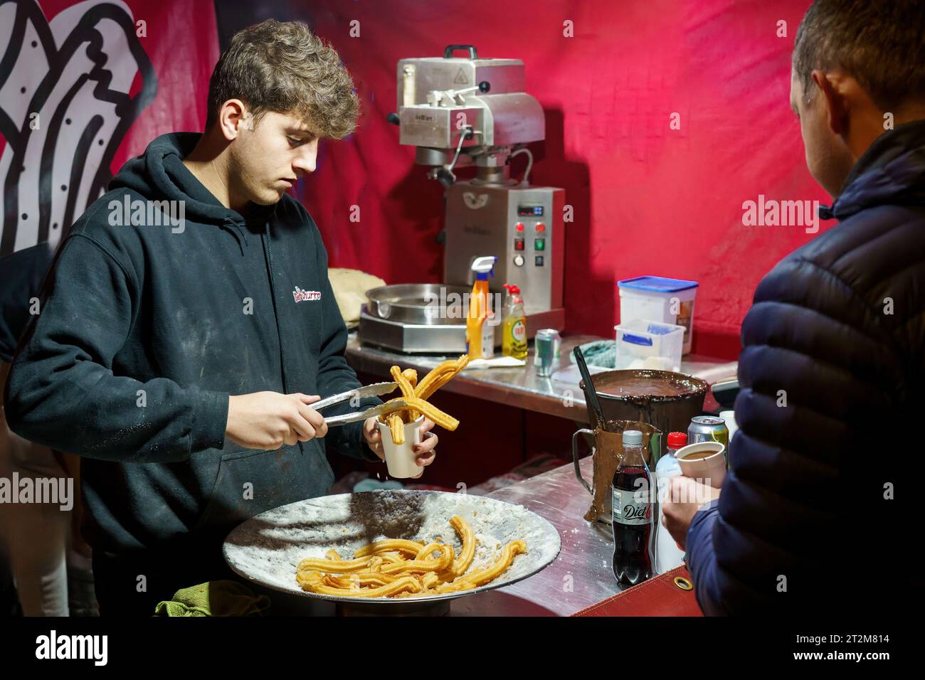 Al maschio vengono serviti churros ricci con salsa di cioccolato in una tazza, preparati al momento in un wok presso un mercatino di Natale, Harrogate, Yorkshire, Regno Unito. Foto Stock