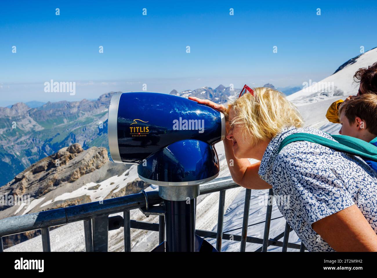 Un turista guarda attraverso un telescopio di osservazione sulla cima del Titlis, una montagna nelle Alpi Uri tra i cantoni di Obwalden e Berna sopra il villaggio di Engelberg Foto Stock