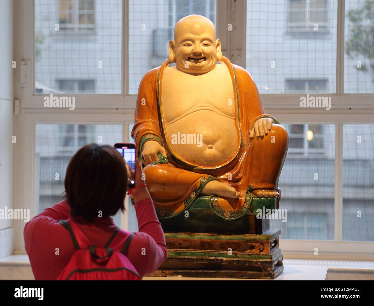 Una donna scatta una foto del Buddha di porcellana della dinastia Ming al British Museum di Londra, Regno Unito Foto Stock