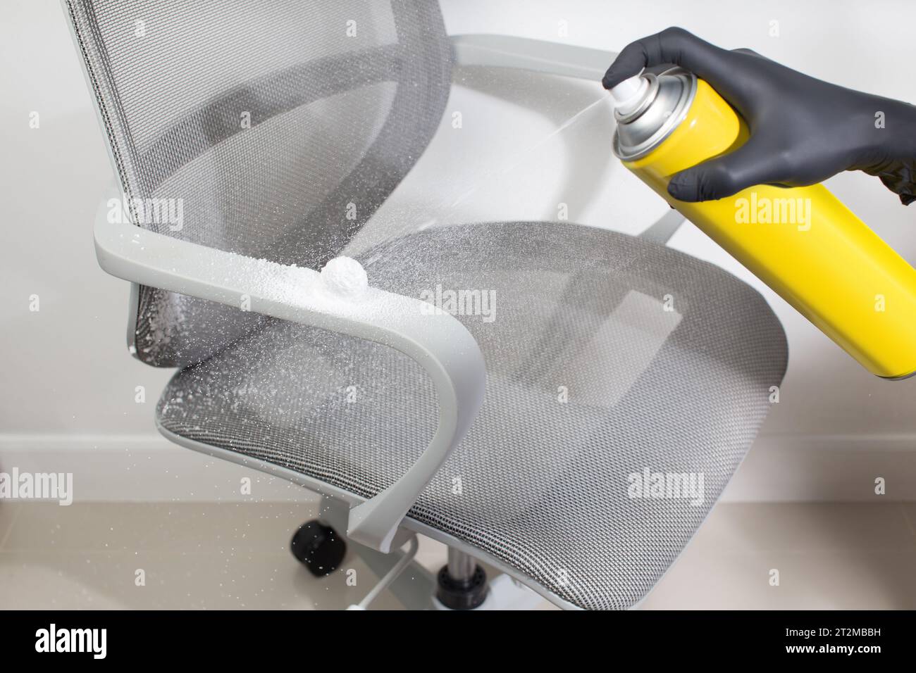 L'uomo che indossa guanti neri spruzza detergente in schiuma multiuso sul bracciolo della sedia per pulirlo. Foto Stock