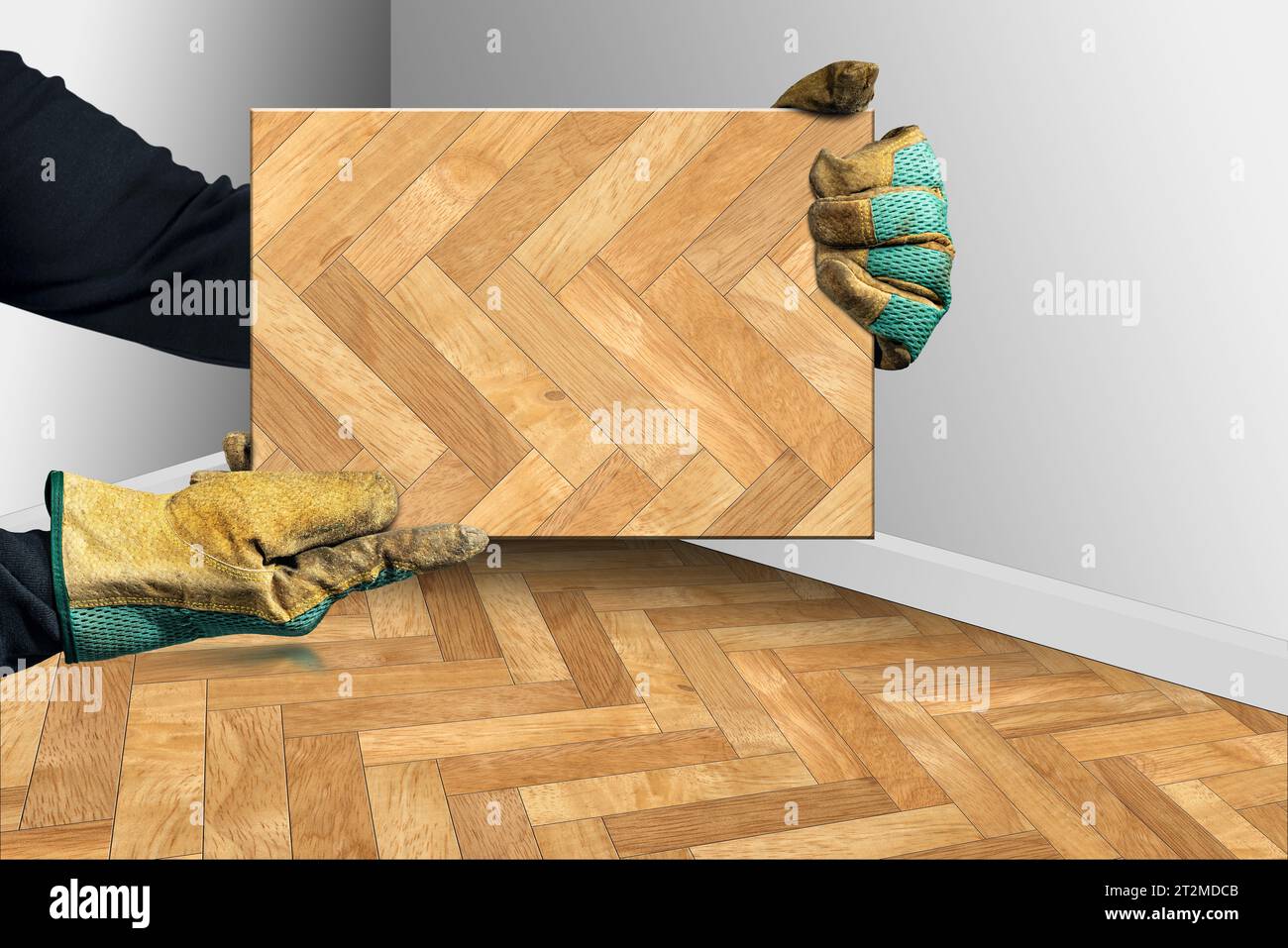 Lavoratore manuale con guanti da lavoro protettivi che contengono un campione di parquet a spina di pesce, angolo di una stanza con parquet in legno a spina di pesce e pareti bianche Foto Stock