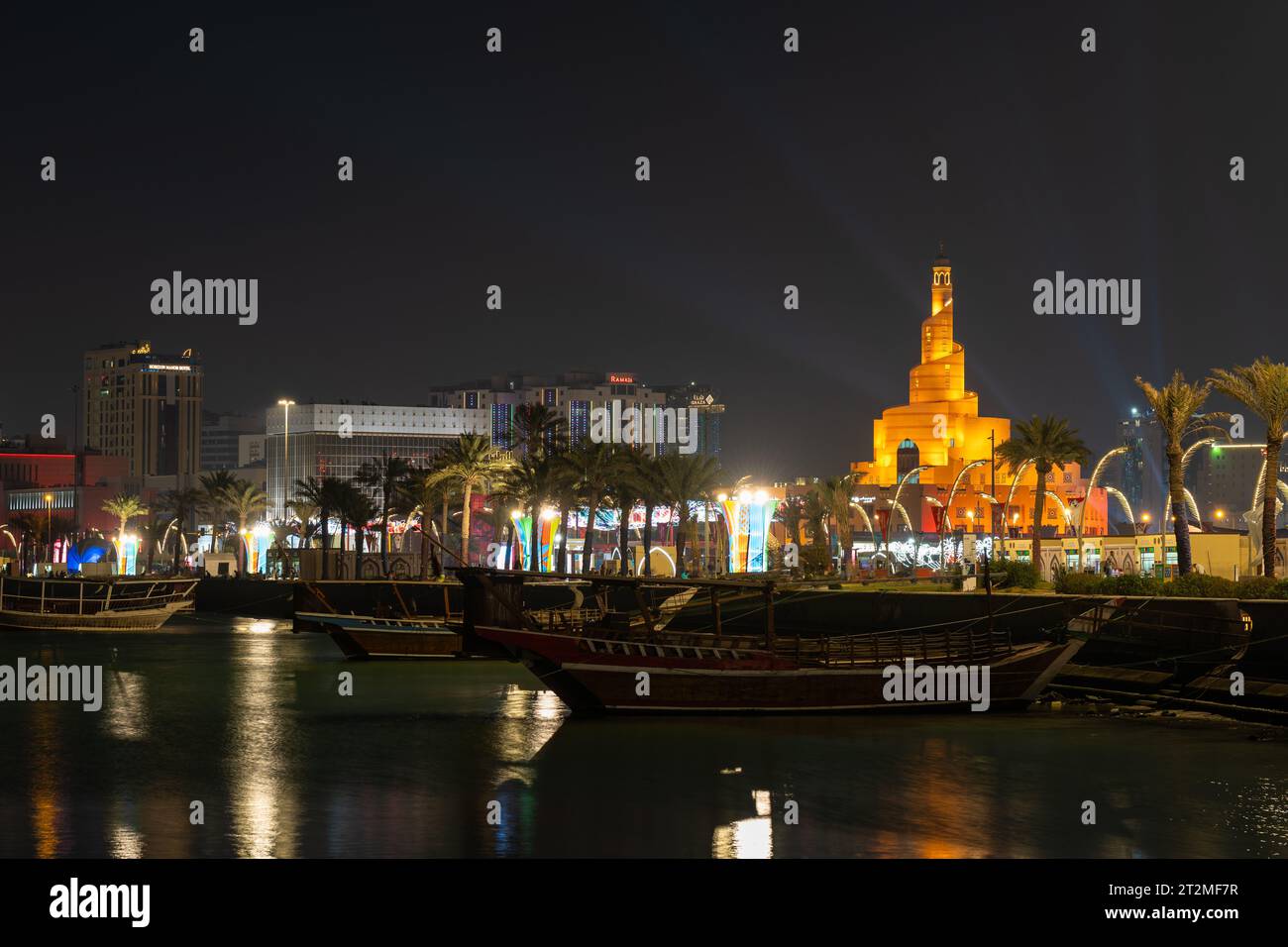 Doha, Qatar - 3 dicembre 2022: Tradizionale dhow in legno ancorato al porto di Dhow nella baia di Doha con moschea a spirale e minareto sullo sfondo. Visualizza da Foto Stock