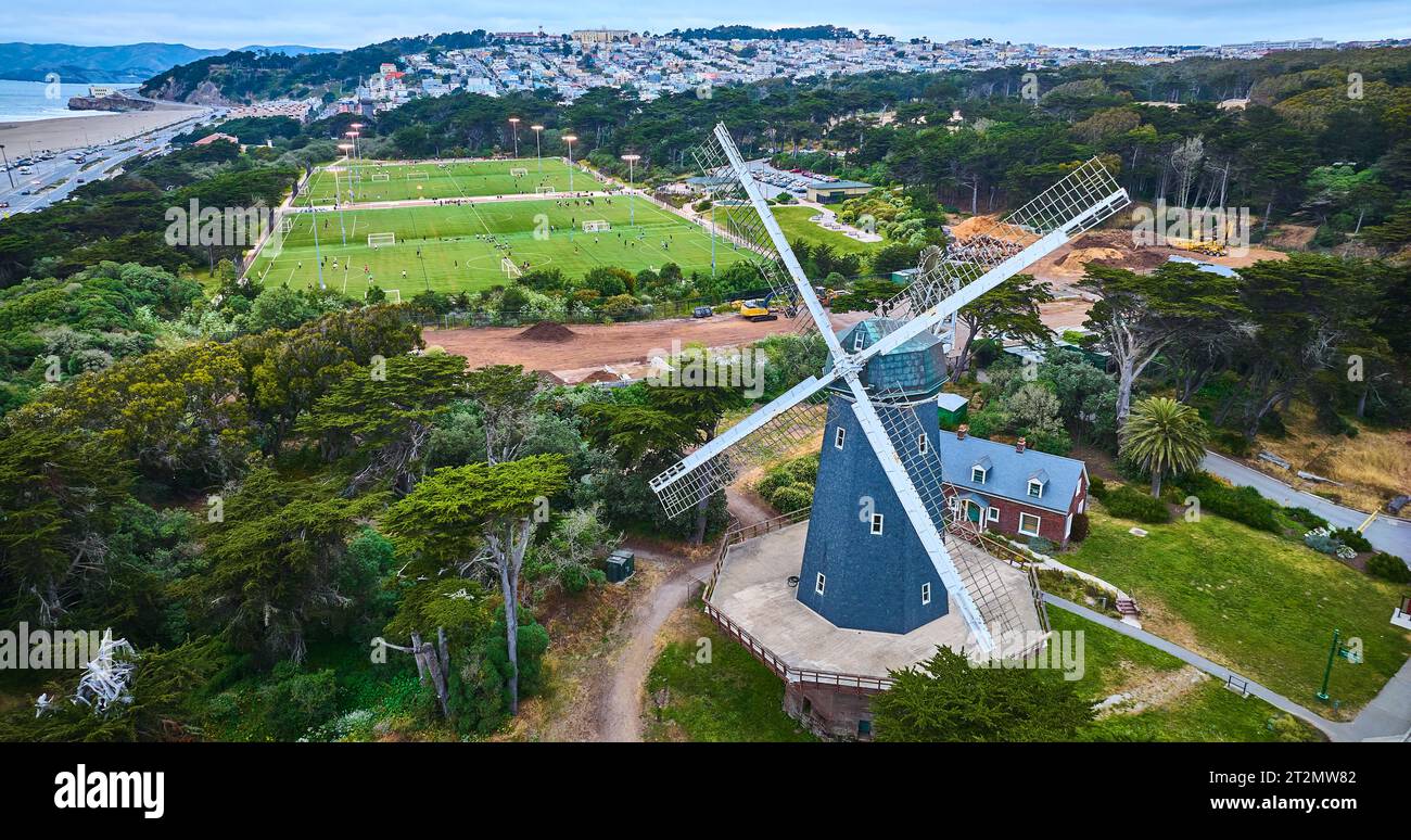 Mulino a vento murphy blu con pale bianche e campo da calcio dietro di esso con grande città Foto Stock