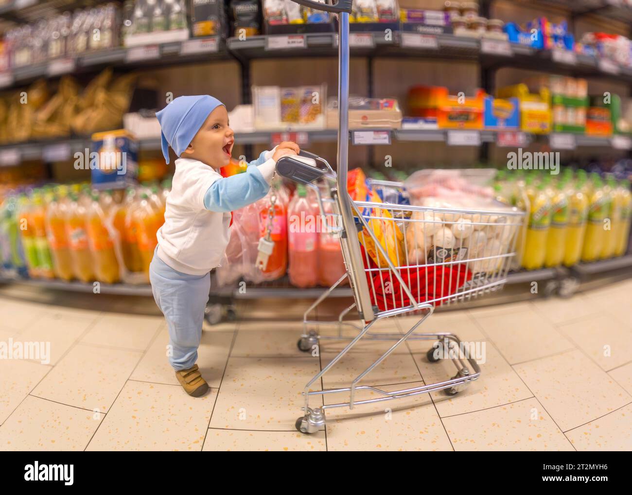 18 ottobre 2023-Bucarest-Romania-adorabile e felice bambino che ha appena imparato a camminare riempì il cestino della spesa per bambini con tutti i tipi di prodotti Foto Stock