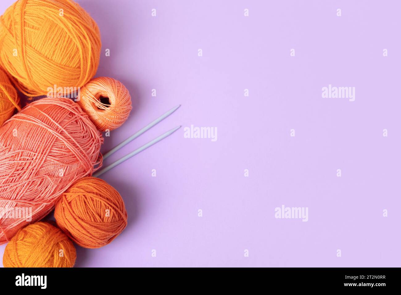 Layout creativo composto da fili arancioni e rosa per lavorare a maglia su uno sfondo lilla con spazio per il testo. Maglieria con ricci per hobby. Concetto fallo Foto Stock