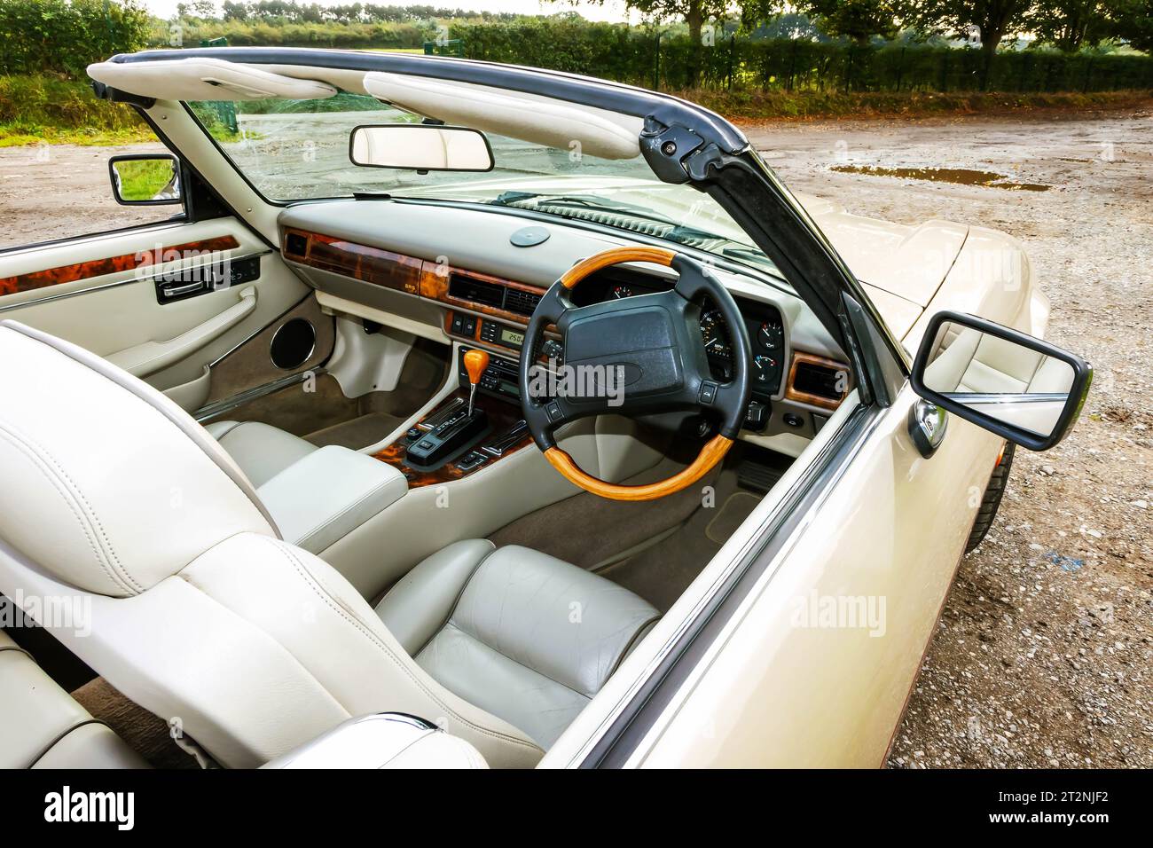 Cabina di pilotaggio di una Jaguar XJS convertibile con capote in un parcheggio in ghiaia nel paese Foto Stock