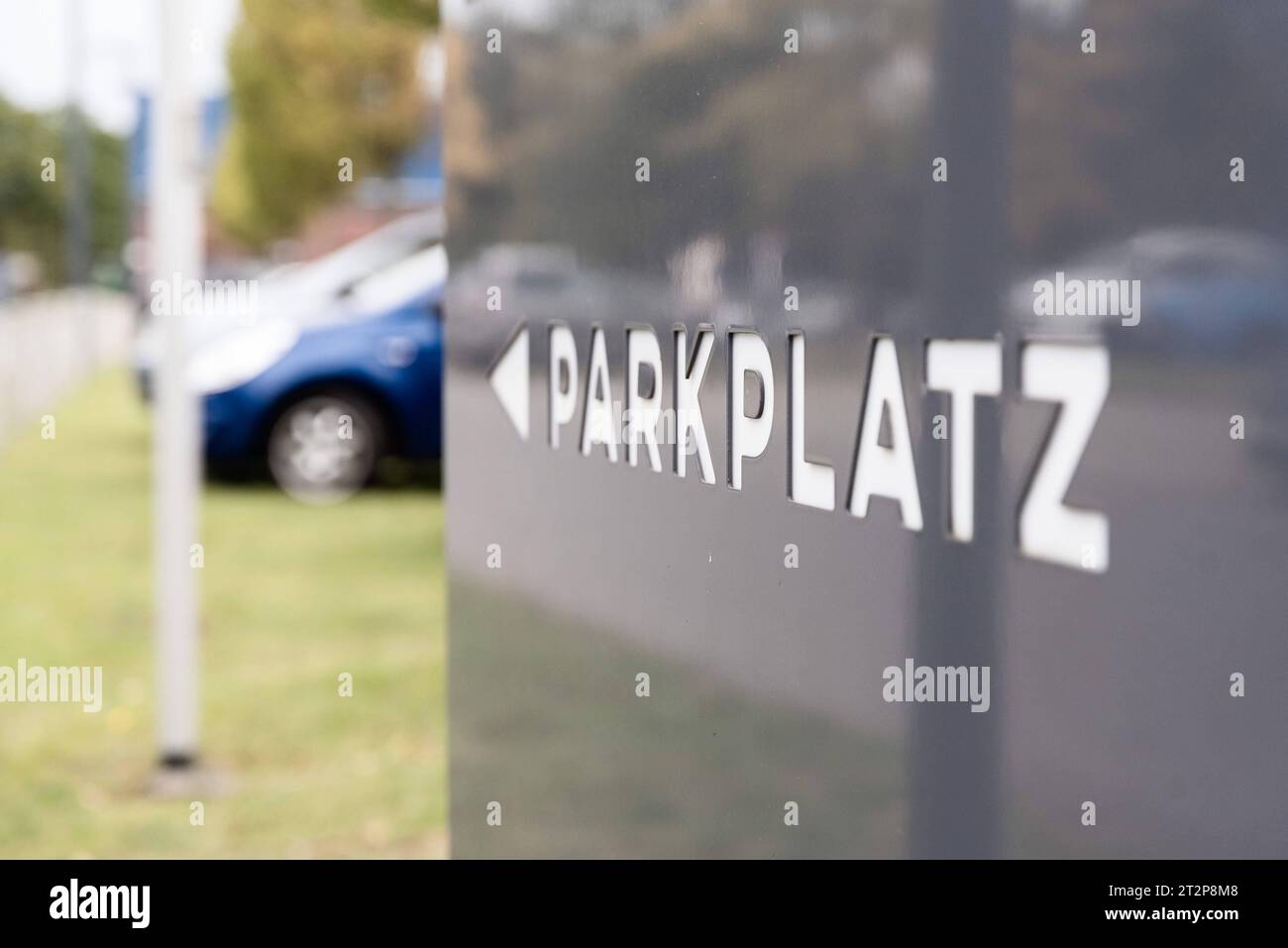 Parkplatz - Wegweiser, Torneum Fußballpark, F.C. Union Tornesch, 08.10.2023 /// Weiße ausgestanzte Buchstaben in einer grauen Metallsäule bilden den Schriftzug PARKPLATZ . IM Schild spiegelt sich die Auffahrt mit den Bäumen. Hinten stehen PKWs auf dem Rasen. Schleswig-Holstein Deutschland 231008 RS-1-016441 DSC 6236 *** cartello di parcheggio, Torneum Fußballpark, F C Union Tornesch, 08 10 2023 lettere bianche punzonate in una colonna di metallo grigio formano la scritta PARKPLATZ il cartello riflette il vialetto con gli alberi dietro ci sono auto sul prato Schleswig Holstein Germania 231008 RS 1 016441 DSC 6236 Foto Stock