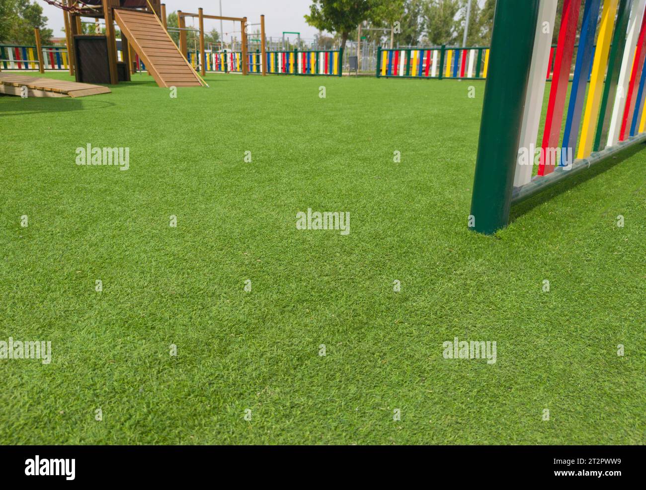 Pavimento in erba verde artificiale nel parco giochi. File colorate di pali verniciati disposte intorno Foto Stock