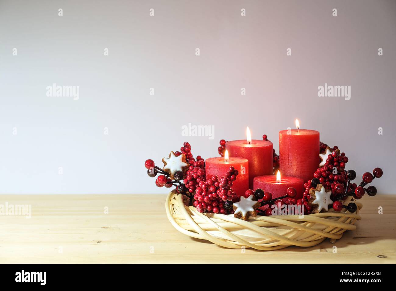 Quarto avvento con quattro candele rosse accese in una corona di vimini di salice naturale con biscotti stellati alla cannella e frutti di bosco artificiali, decorazioni natalizie, copia Foto Stock